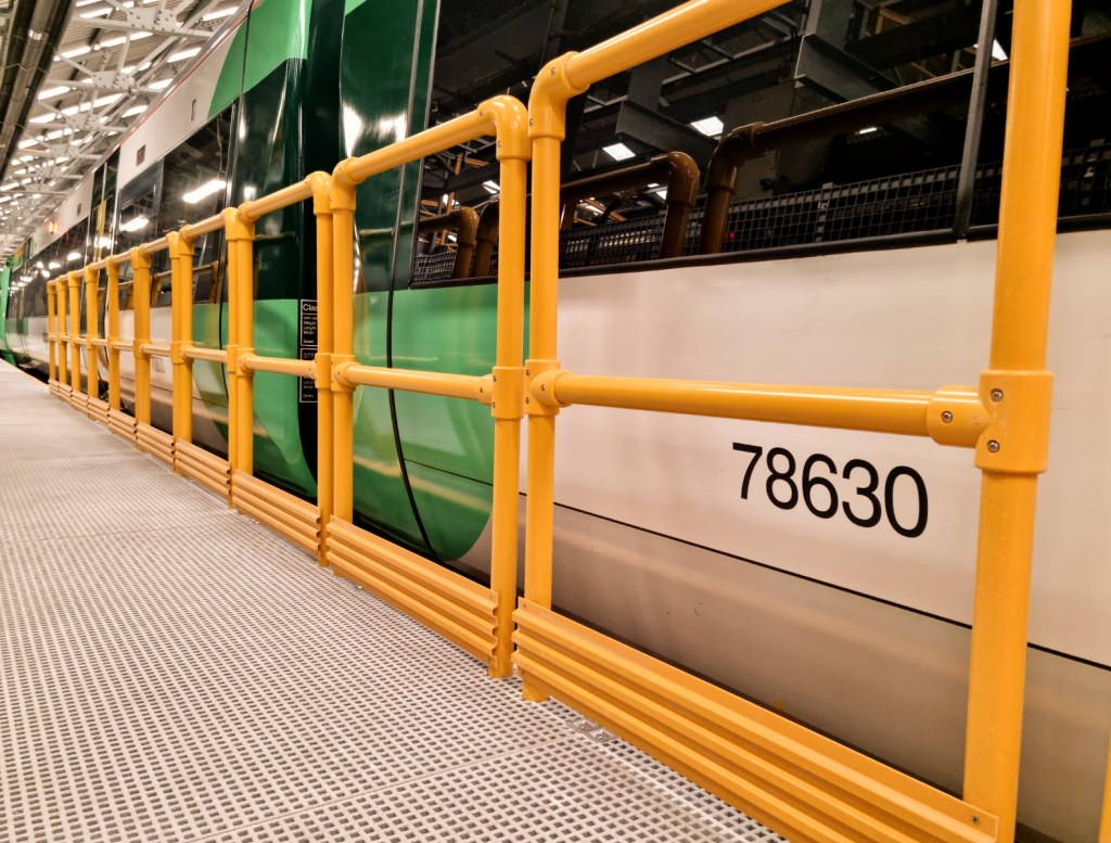 Side view of a green and white train with a visible identification number 78630, enclosed by yellow safety railings in a transportation facility.